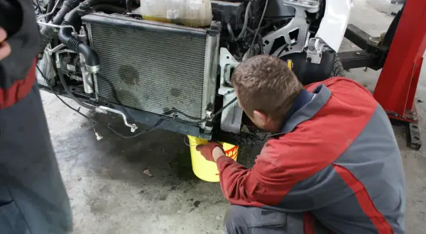 Mechanik w rękawiczkach nalewa płyn do chłodnicy, pokazując, jak działa uszczelniacz do chłodnic.