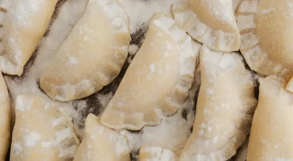 Surowe pierogi posypane mąką, gotowe do blanszowania.