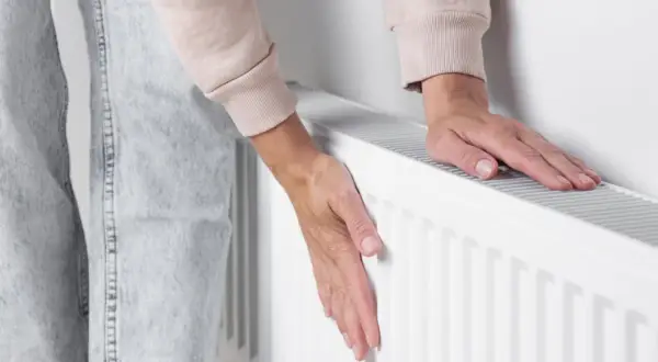 Dłonie sprawdzają temperaturę grzejnika. Jeden pion nie grzeje, co może oznaczać problem z ogrzewaniem.