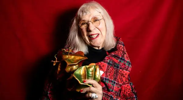 Suzanne på scen, glad och med ett glittrande pris i famnen, klädd i en röd rutig kavaj mot en röd bakgrund.