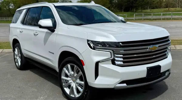 Biały Chevrolet Tahoe z chromowanymi felgami stoi na drodze, otoczony zielenią i chmurami.
