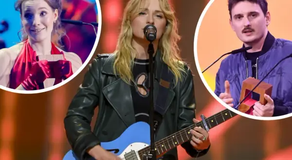 Trzy osoby na scenie: kobieta gra na gitarze, kobieta w czerwieni trzyma nagrodę, mężczyzna z wąsami trzyma nagrodę.