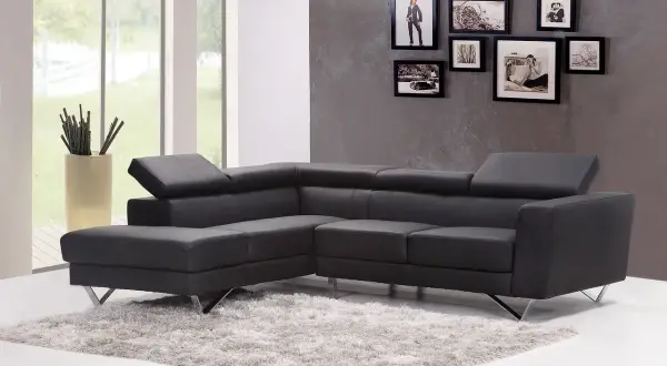 Divano angolare in pelle grigio antracite scuro, con tappeto soffice e cornici decorative alle pareti.