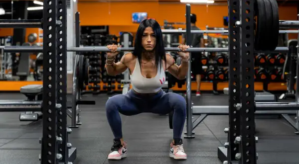 Donna determinata esegue uno squat a casa con bilanciere, concentrata sul suo allenamento.