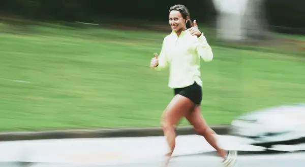 Donna sorridente corre con pollice in su, indicando un ottimo ritmo medio corsa.
