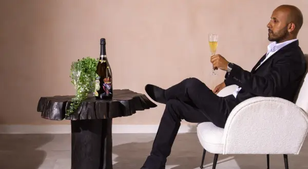 Mann in schwarzem Anzug genießt ein Glas Sekt neben einer Flasche, die wie der teuerster Sekt der Welt aussieht.
