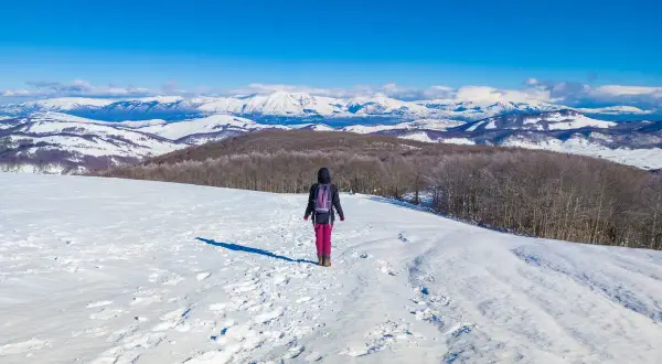Escursionista in un paesaggio innevato, ideale per scoprire dove andare sulla neve vicino Roma. Montagne imbiancate all'orizzonte.