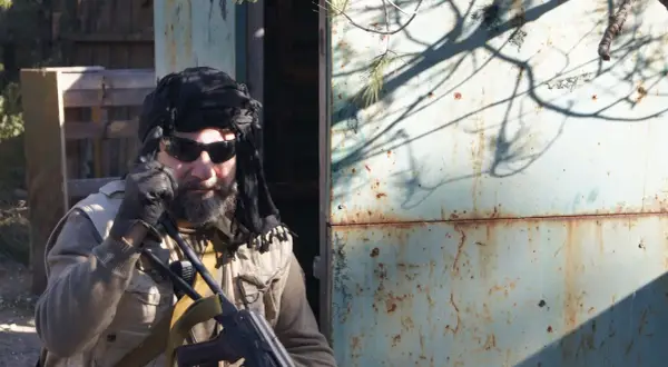 Hombre con turbante negro, gafas de sol y chaleco táctico, listo para una partida de milsim airsoft.