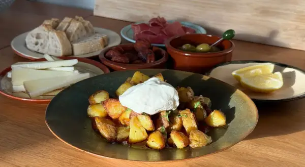 En tallrik med krispiga patatas bravas toppad med en klick krämig sås, omgiven av bröd, ost, chorizo, oliver och citronklyftor.