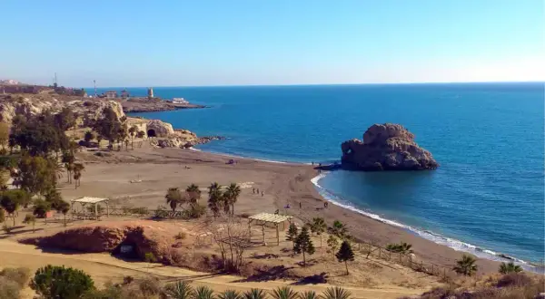 La playa Peñón del Cuervo, con su icónica roca en el mar, invita a pasear por su arena oscura bajo un cielo azul.