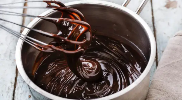 Ein Schneebesen rührt glänzende, dunkle schoko ganache in einem Topf.