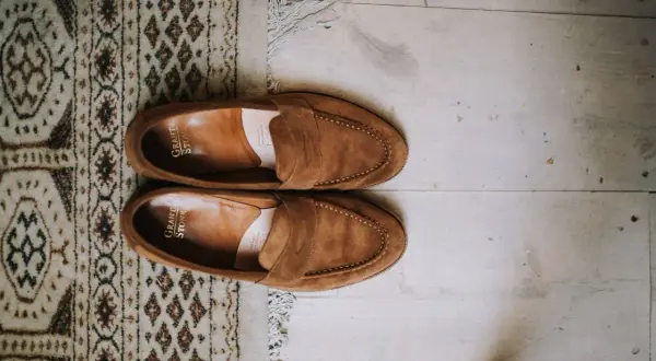 Une paire de mocassins en daim marron, posée sur un tapis à motifs et un parquet. Idéal pour raviver la couleur du daim naturellement.