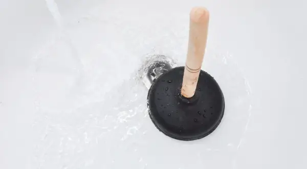 Ventouse sur un drain de baignoire avec de l'eau qui coule. Une solution simple pour savoir comment déboucher une baignoire rapidement.