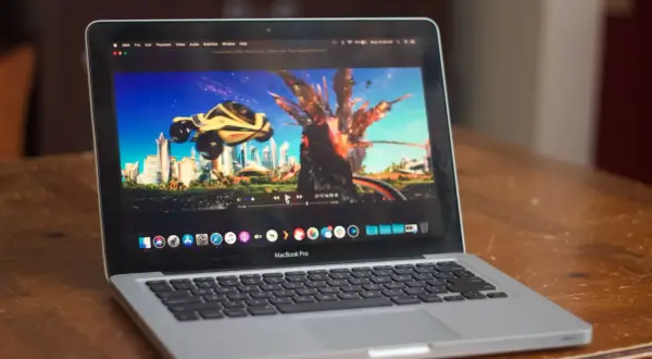 A MacBook Pro displays the "Speed Racer" trailer on the IINA player, showing a futuristic city and a car mid-explosion.