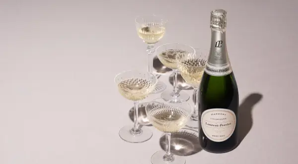 Laurent-Perrier Champagnerflasche mit gefüllten Gläsern. Die Dosage Champagner Bedeutung liegt in der perfekten Balance.