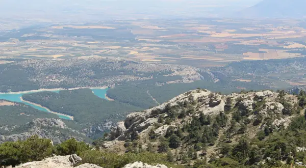 Vistas panorámicas de la sierra de Cazorla, Segura y Las Villas, con un embalse turquesa y campos cultivados al fondo.