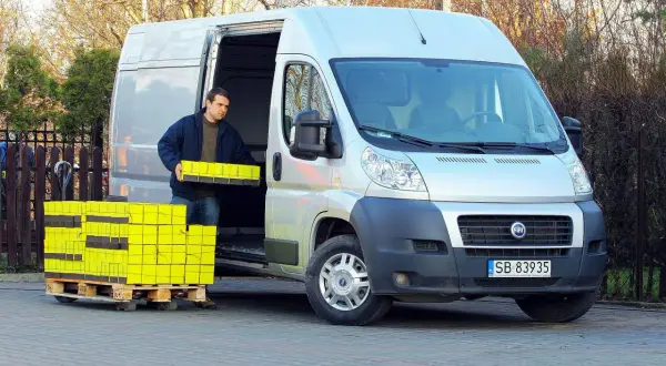 Mężczyzna rozładowuje żółte paczki z furgonetki Fiat Ducato 2.3.