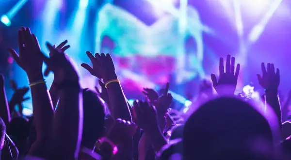 Mani alzate in un'atmosfera elettrica durante un rave party in Francia. Luci viola e blu illuminano la folla in estasi.