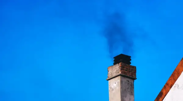 Dym z komina, być może dzięki zastosowaniu filtra kominowego zamiast wymiany pieca, unosi się na tle błękitnego nieba.
