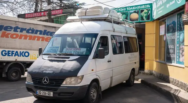 Biały bus z napisem "BORJOMI AKHALTSIKHE" na przedniej szybie, gotowy do podróży. To może być Twój sposób, jak dojechać z Kutaisi do Batumi, jeśli cel podróży jest inny.