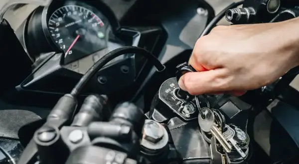 Mano girando la llave de contacto de una moto que se paró en marcha y no arranca. El tablero muestra el velocímetro.