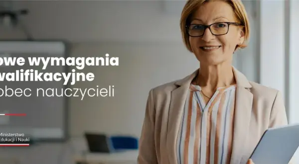 Uśmiechnięta nauczycielka w okularach trzyma tablet w sali lekcyjnej.