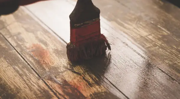 Brocha aplicando una capa de imprimación sobre tablones de madera rústica, preparándolos para un nuevo acabado.