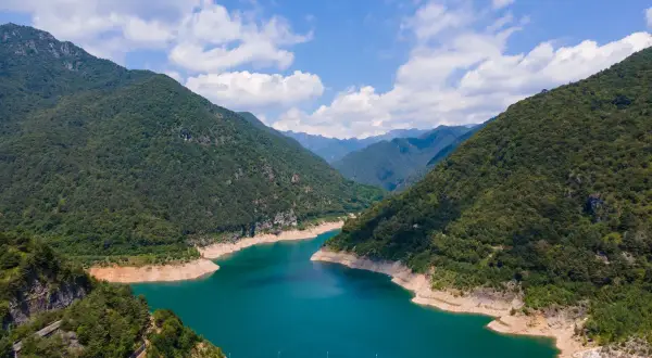 Imponente diga sul lago di Valvestino, circondato da montagne verdi e un cielo azzurro con nuvole bianche.