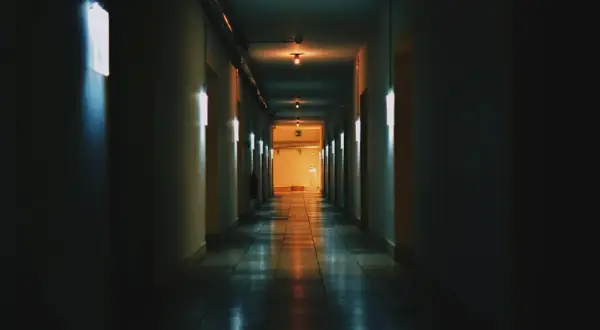 Un corridoio buio con luci al neon che cercano di rendere luminoso lo spazio. La prospettiva crea un senso di profondità.