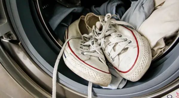 Weiße Turnschuhe mit roten Streifen liegen in der Waschmaschine, bereit zum Laufschuhe waschen.