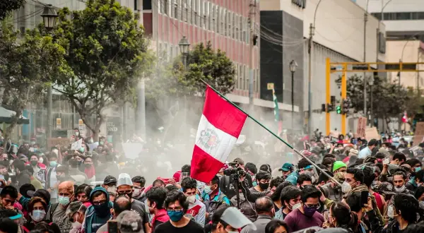Tłum ludzi na ulicy w Peru, z flagą narodową i dymem. Czy w Peru jest bezpiecznie? Trudno ocenić po tym zdjęciu.