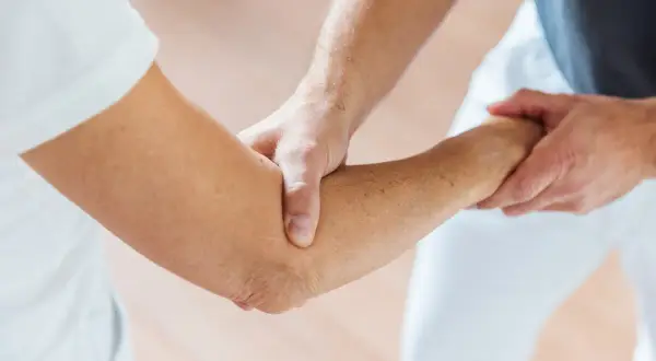 Physiotherapeut hilft beim Ellenbogen mobilisieren nach OP. Sanfte Berührung zur Wiederherstellung der Beweglichkeit.