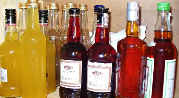 Rząd butelek z różnymi alkoholami, w tym żółtymi nalewkami i ciemnymi, jak czarna wódka.