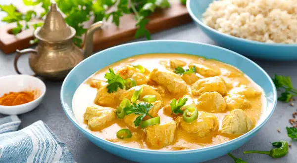 Aksamitny kurczak curry po tajsku w niebieskiej misce, udekorowany kolendrą i papryczką chili. Obok ryż i przyprawy.