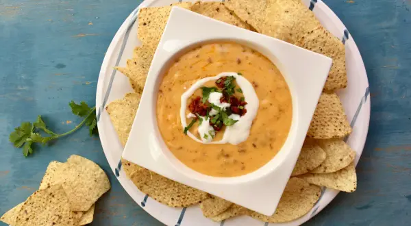 Salsa de queso cremosa en un tazón blanco, rodeada de totopos y adornada con crema y cilantro.