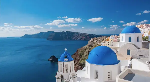 Blaue Kuppeln und weiße Gebäude auf Santorini, ein Traumziel für Griechenland Reisetipps. Die Caldera im Hintergrund.