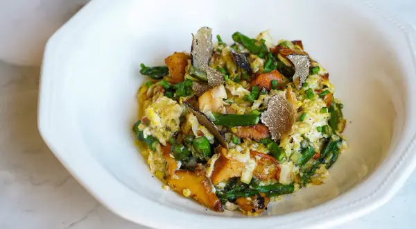 Delicioso revuelto de cantharellus con espárragos, trufa negra y cebollino, servido en un plato blanco.