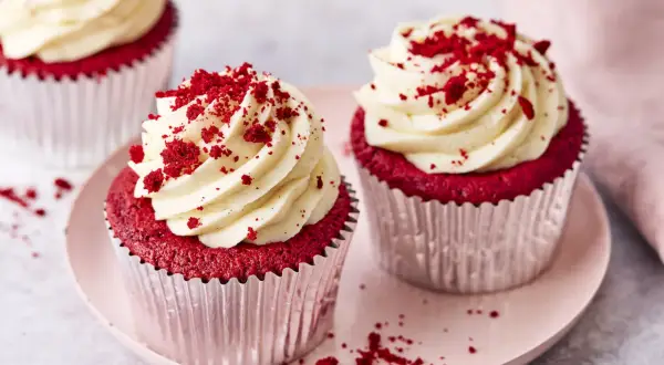 Zwei köstliche red velvet cupcakes mit cremiger Glasur und roten Krümeln, auf einem rosa Teller.