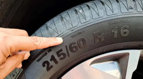 Palec wskazuje na oznaczenia opon: 215/60 R16. Informacje te pomagają dobrać odpowiednie ogumienie.