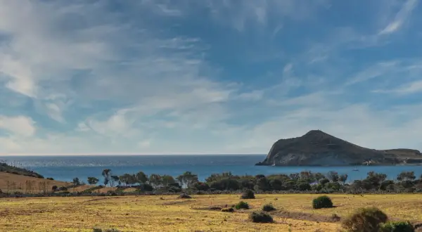 Paisaje árido del desierto Cabo de Gata con mar azul y una isla rocosa al fondo.