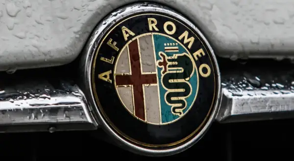 Klasyczne alfa romeo logo z krzyżem i wężem, błyszczące mimo kropel deszczu na karoserii.