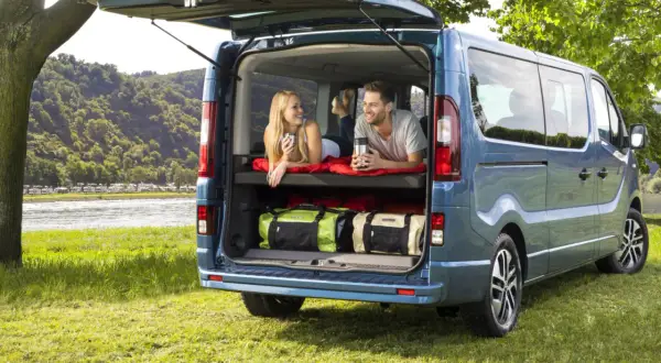 Para relaksuje się w kamperze Opel Vivaro, z widokiem na rzekę i kemping.