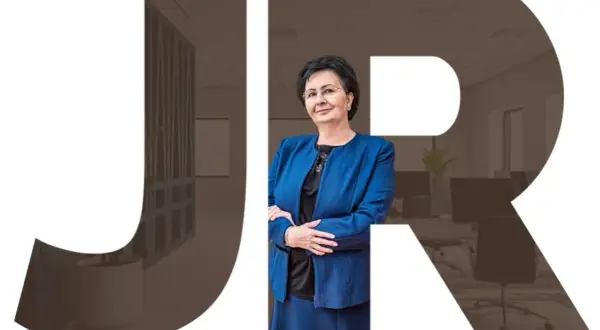Kobieta w niebieskiej marynarce na tle biura, z literami JR.