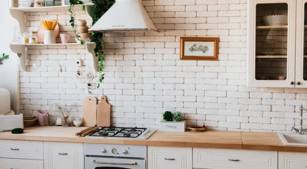 Inspiracja do tego, jak zrobić blat kuchenny z płytek ceramicznych. Jasna kuchnia z drewnianym blatem, białą cegłą i roślinami.