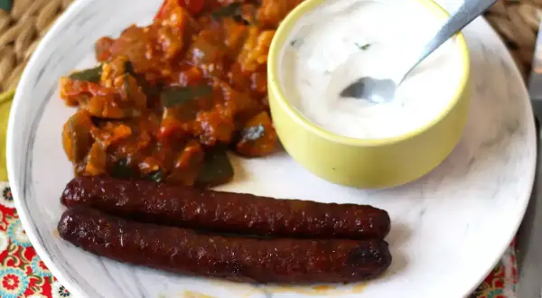 Dos salchichas merguez que es picantes, acompañadas de un guiso de verduras y una salsa cremosa.