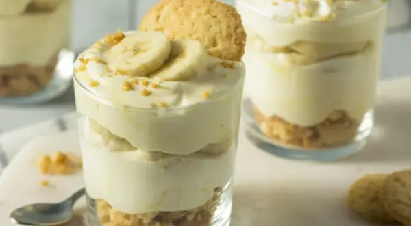 Warstwowy deser z twarogu, bananów i ciasteczek, udekorowany plasterkami banana i okruszkami.