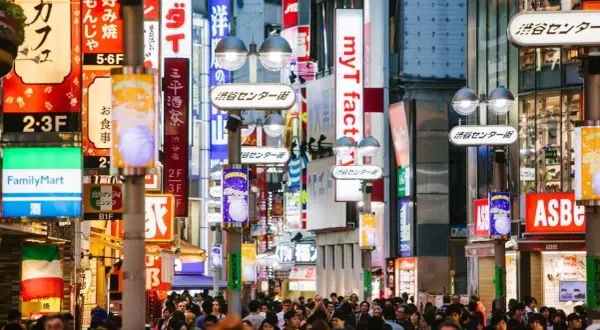 Tłoczna ulica Shibuya w Tokio, jednym z najczęściej odwiedzanych miast świata, pełna neonów i sklepów.