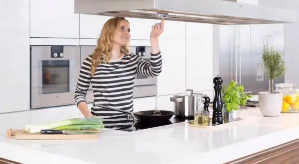 Junge Frau bedient Dunstabzugshaube mit Herd-Abschaltautomatik. Sicheres Kochen für Senioren.
