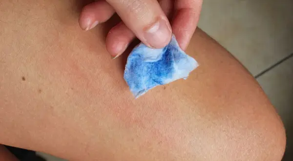 Mano che pulisce la pelle con un dischetto di cotone blu, mostrando come togliere la vernice dalla pelle in modo efficace.