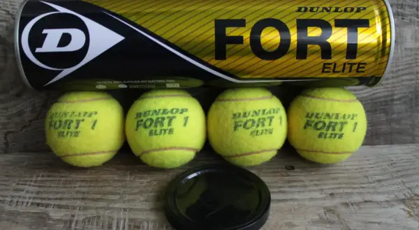 Lattina Dunlop Fort Elite e quattro palline da tennis gialle su fondo in legno. Pronte per una partita!